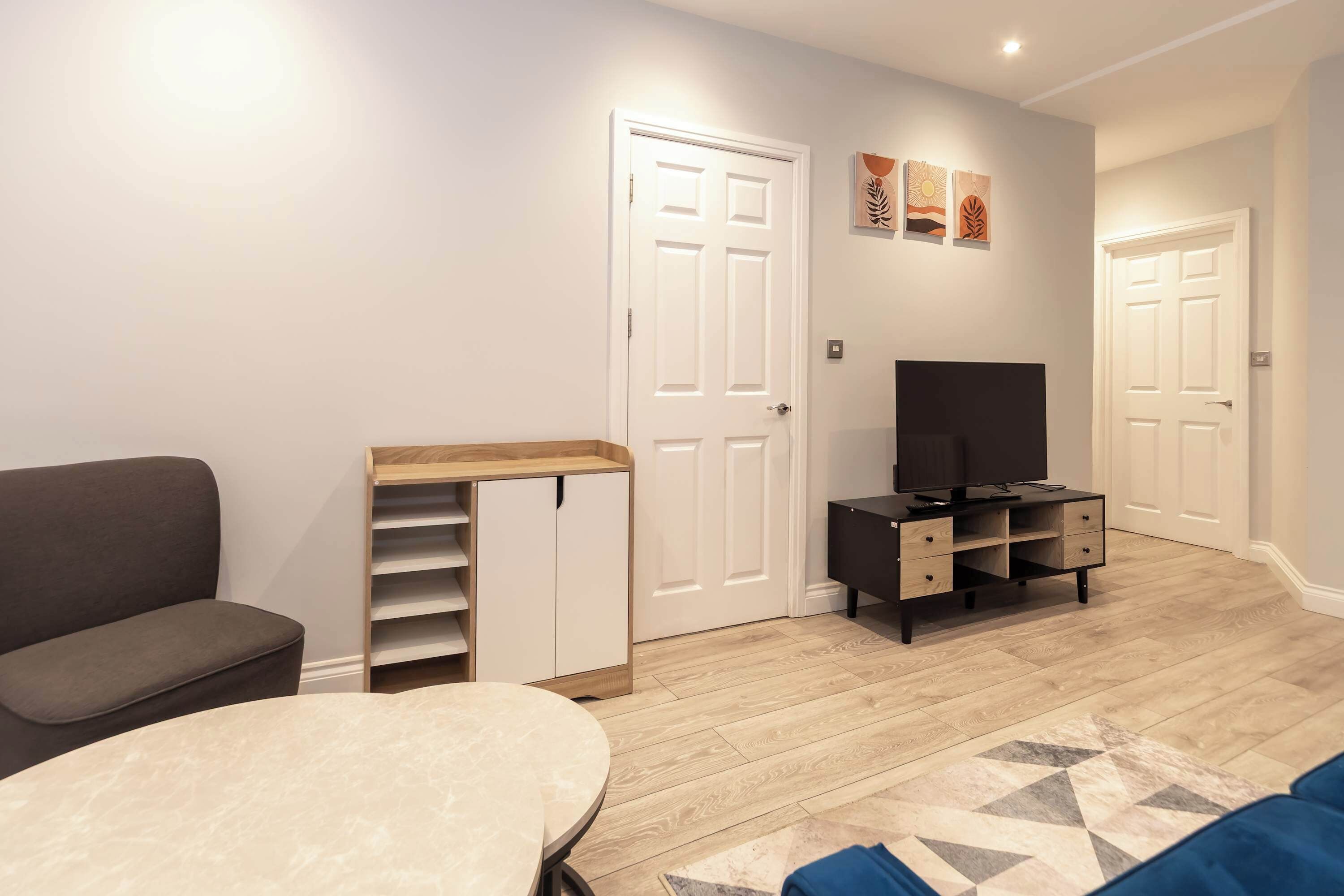 Een moderne woonkamer met een grijze bank, een ronde tafel, een tv-meubel en een houten kast.