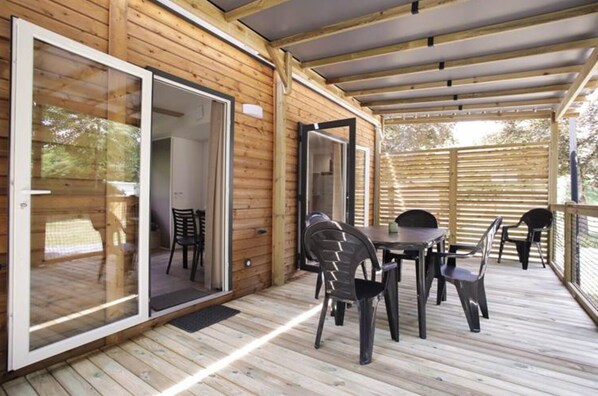A wooden deck with a table and chairs, a sliding glass door, and a covered area with a roof. - Le Florenville Camping (Florenville)