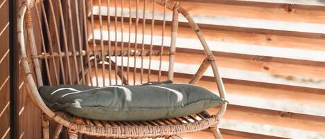 A wicker chair with a cushion against a wooden wall with horizontal slats.