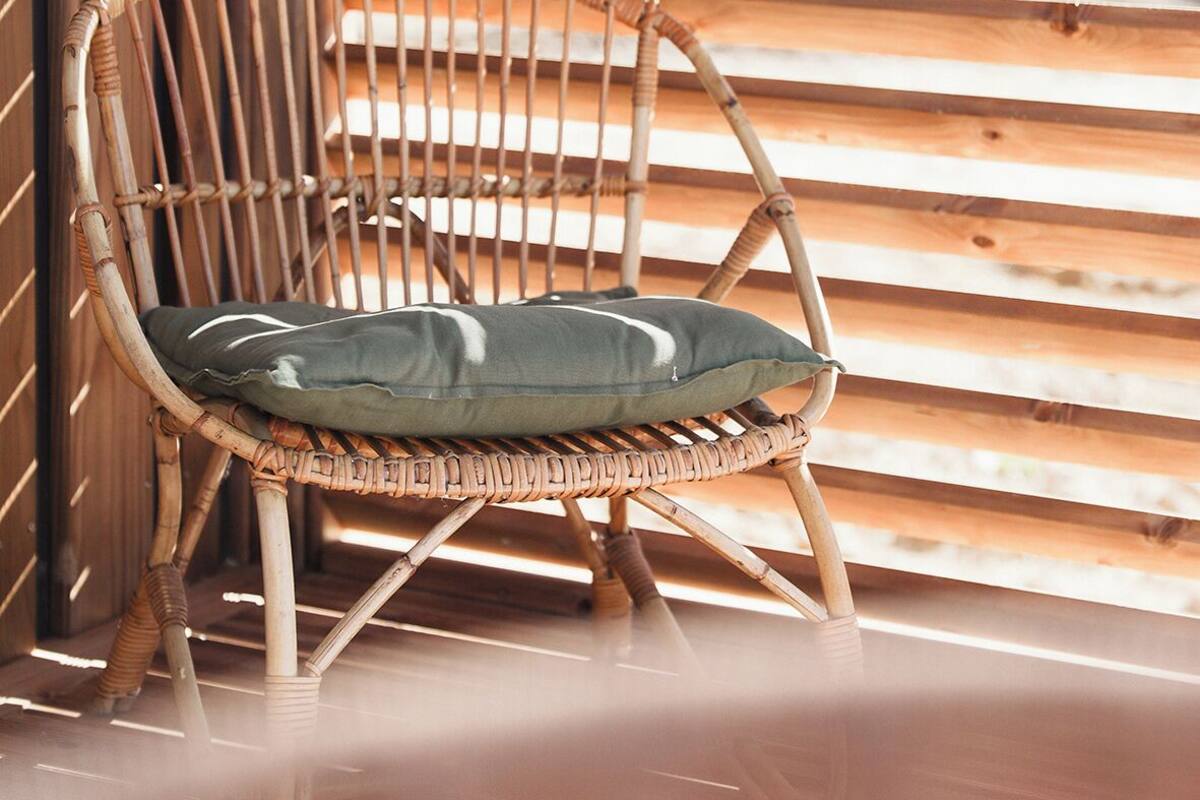 Una silla de mimbre con cojín apoyada en un muro de listones de madera.