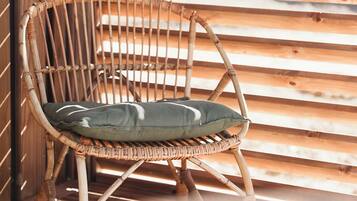 A wicker chair with a cushion against a wooden slatted wall.