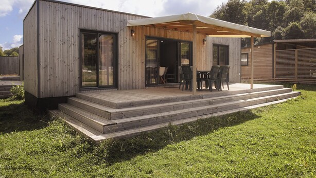 Una casa moderna de fusta amb un porxo cobert, mobiliari exterior i una escala que condueix a l'entrada.