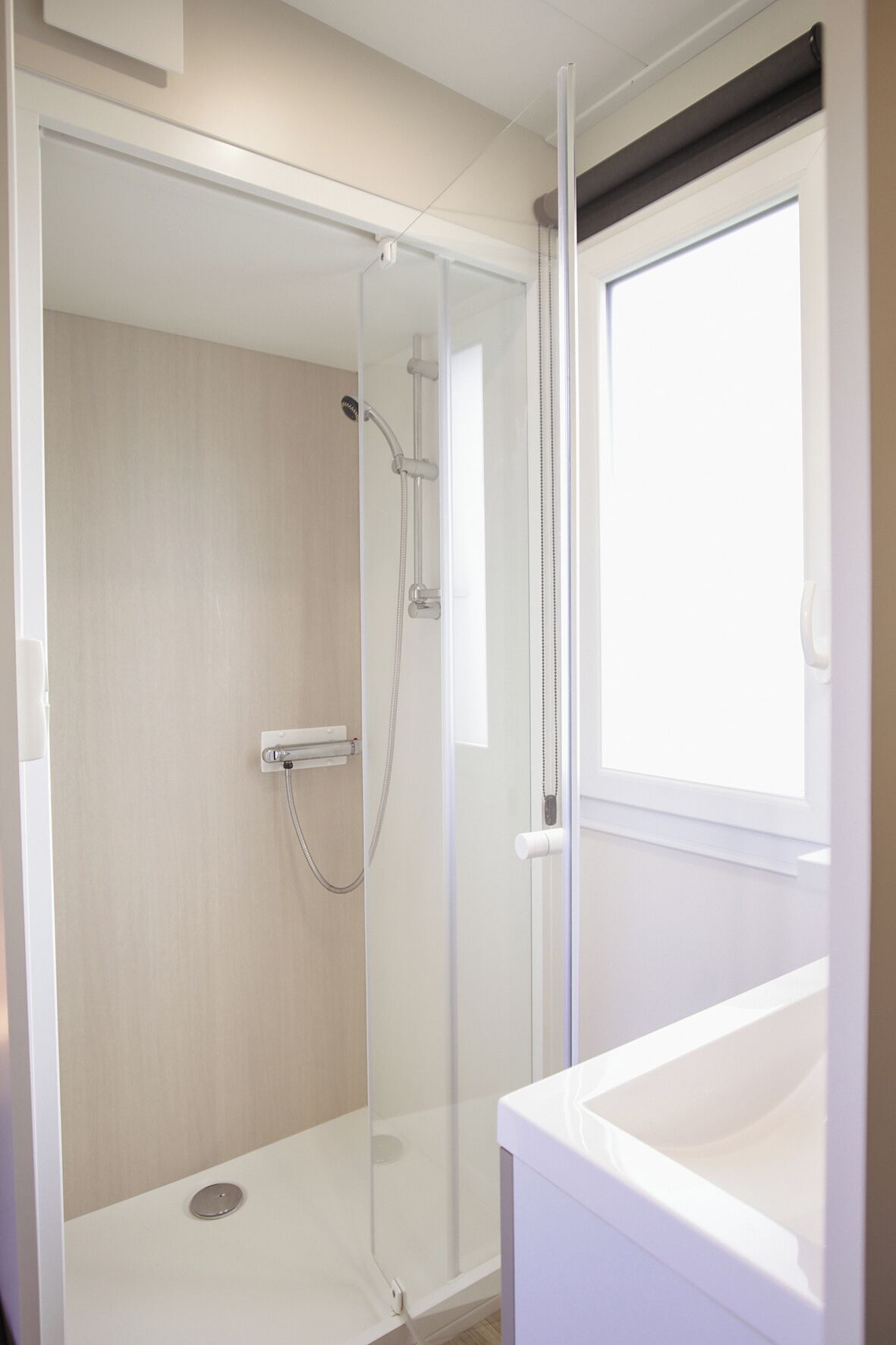 Un baño moderno con cabina de ducha de vidrio, un lavabo blanco y una ventana que proporciona luz natural.