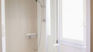 Un baño moderno con cabina de ducha de vidrio, un lavabo blanco y una ventana que proporciona luz natural.