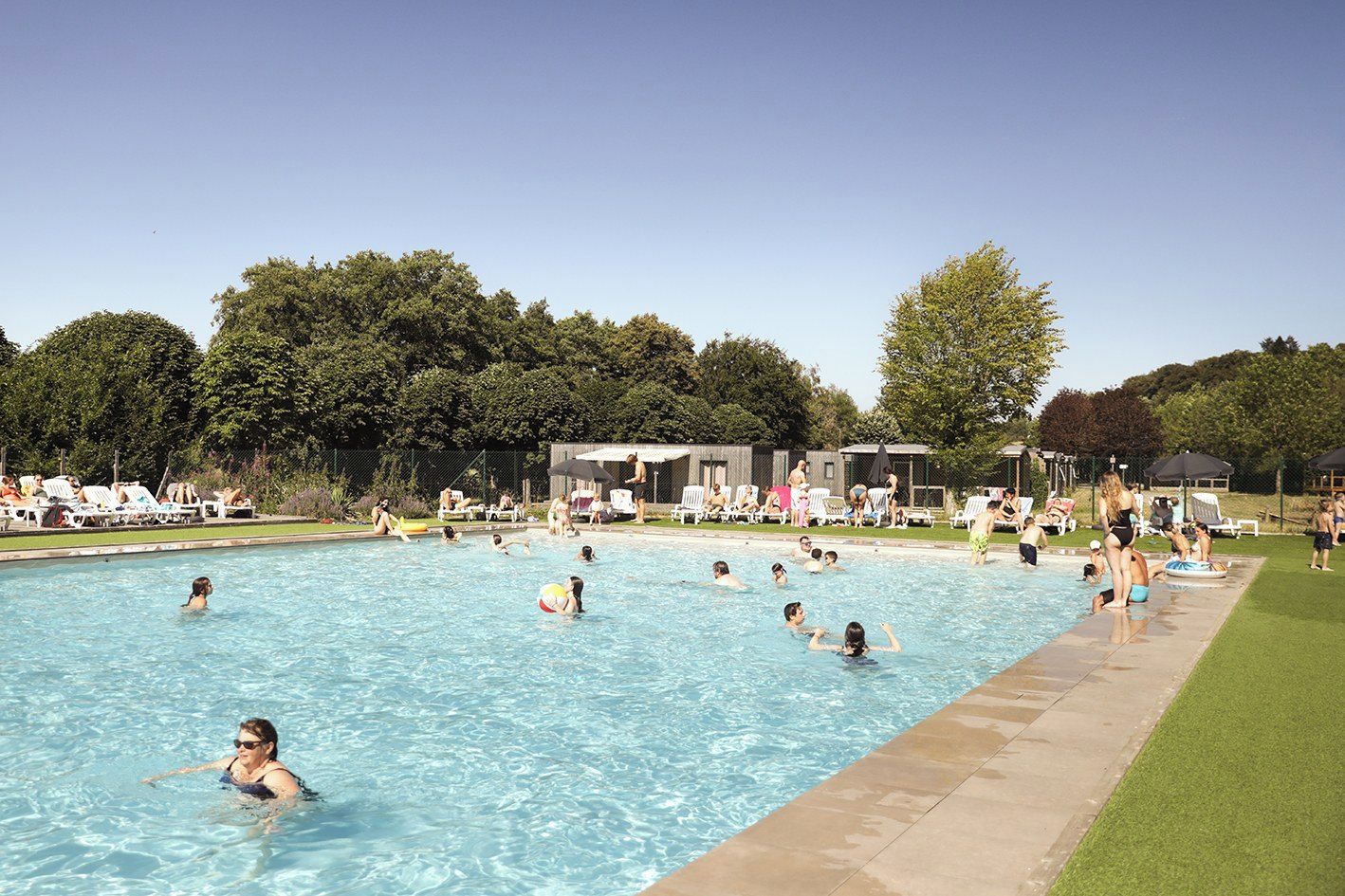 Een zwembad met mensen in het water, omringd door ligbedden en parasols.