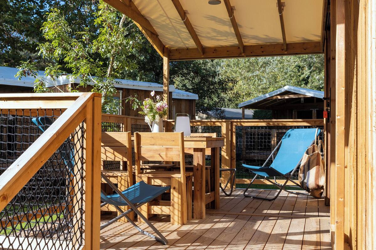 Una terraza de madera con un espacio de estar cubierto, una mesa y una silla.