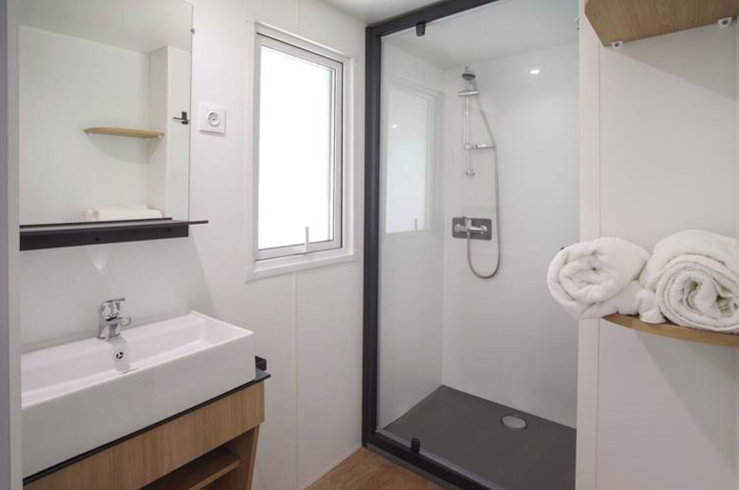 Un bagno moderno con un lavandino bianco, una doccia con pareti in vetro e una finestra.