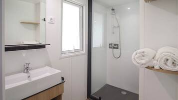 Un bagno moderno con un lavandino bianco, una doccia con pareti in vetro e una finestra.