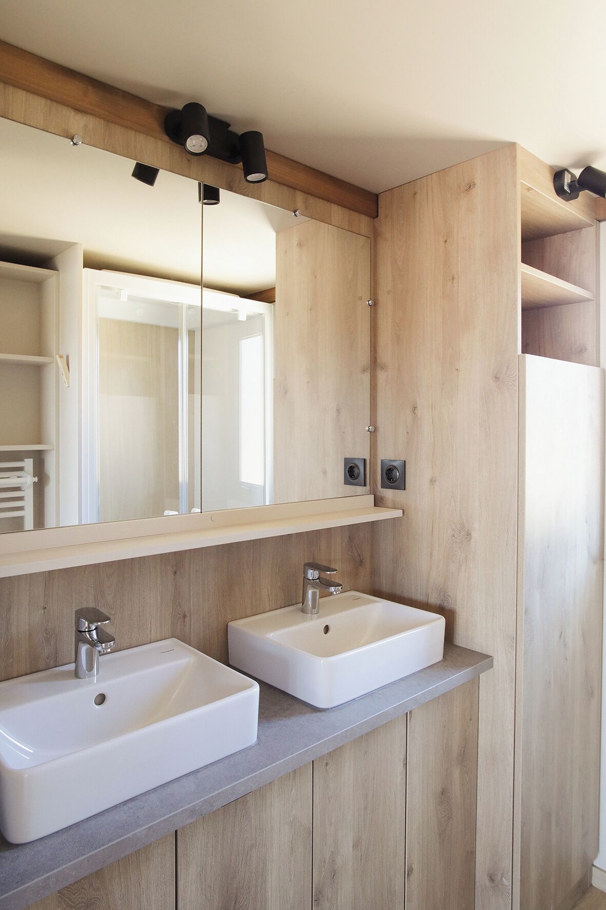 Un baño moderno con paneles de madera, dos lavamanos blancos y un espejo grande.