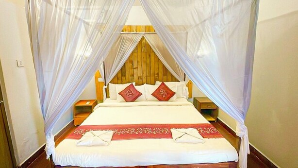 A bed with a canopy, pillows, and a red decorative runner. - Harbor Court Vagator (Vagator)