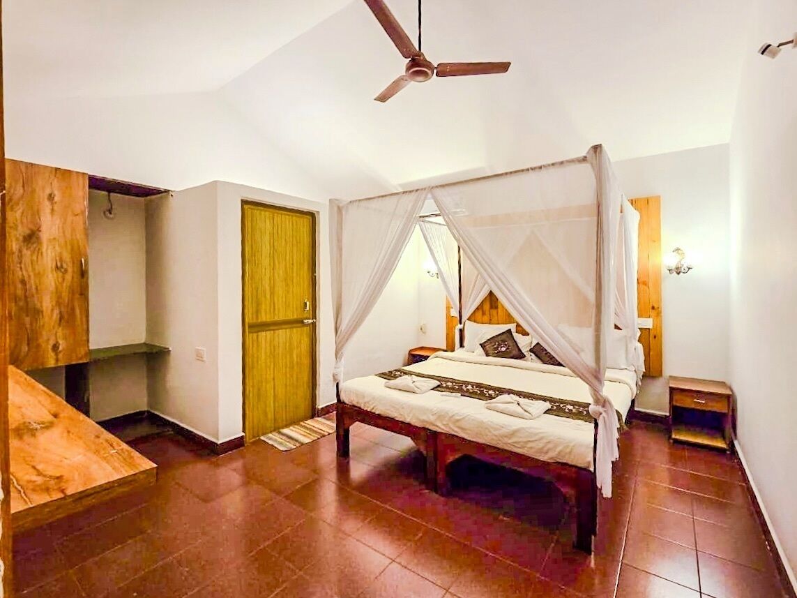 A room with a four-poster bed, a ceiling fan, a wooden wardrobe, and a small bedside table.