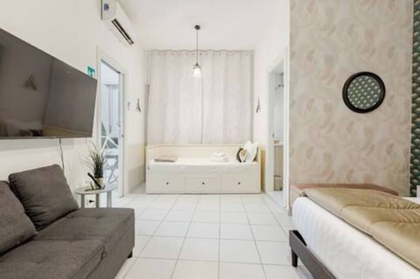 A bedroom with a bed, a sofa, a bedside table, and a mirror.