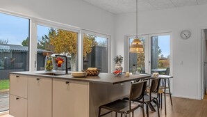 A modern kitchen with a large island, bar stools, and a view of the backyard. - "Barnet" - 180m to the fjord by Interhome (Storvorde)