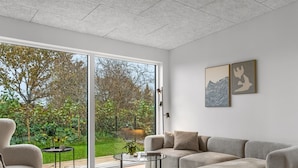 A modern living room with a large sliding glass door leading to a garden, a sofa, a chair, and a coffee table. - "Barnet" - 180m to the fjord by Interhome (Storvorde)