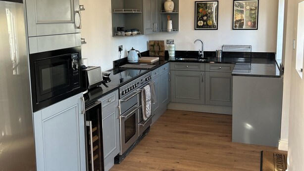 A modern kitchen with grey cabinets, a black countertop, and wooden beams on the ceiling.