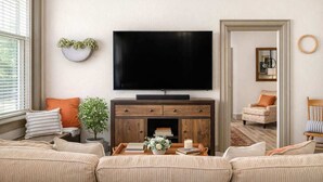 A living room with a large flat-screen TV, a wooden cabinet, a sofa, and a chair. - Stylish Downtown Loft – Free Parking & City Views! (Oshkosh)