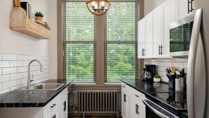 A modern kitchen with white cabinets, a black countertop, a built-in stove, and a window with blinds. - Stylish Downtown Loft – Free Parking & City Views! (Oshkosh)