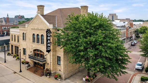 A historic building with a prominent 'GRAND' sign, large windows, and a tree in front. - Stylish Downtown Loft – Free Parking & City Views! (Oshkosh)