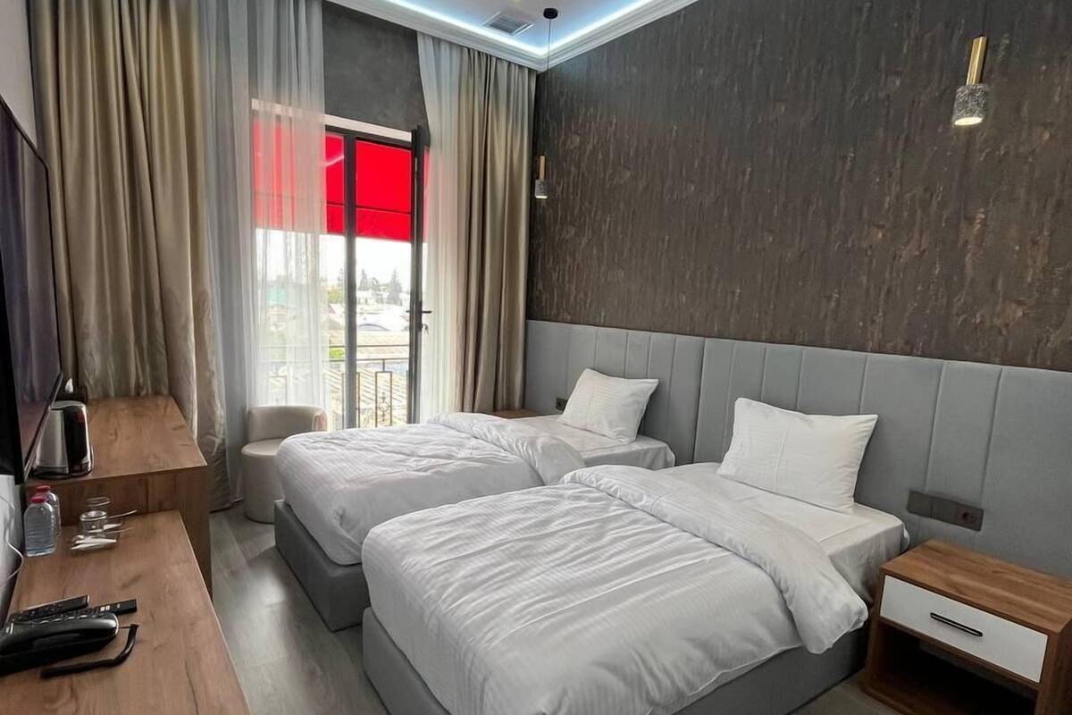 A modern hotel room with two beds, a wooden desk, a TV, and a view of the outdoors.
