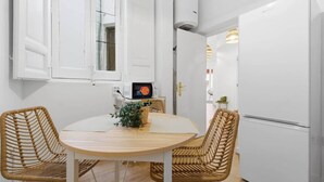 Pieni, käytännöllinen keittiö, jossa on pyöreä pöytä, kaksi rottinkituolia, mikroaaltouuni ja valkoinen jääkaappi.