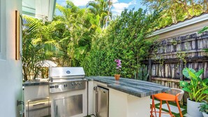 A compact outdoor kitchen with a grill, bar stools, and a potted plant.