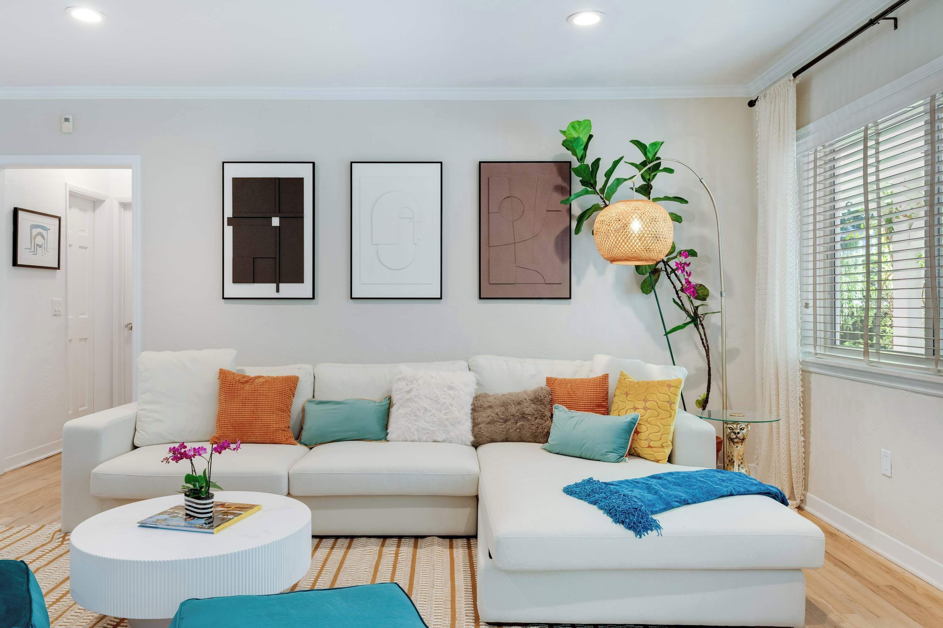 Ein modernes Wohnzimmer mit einem weißen Sofa, einem runden Couchtisch und einem großen Fenster mit Jalousien.