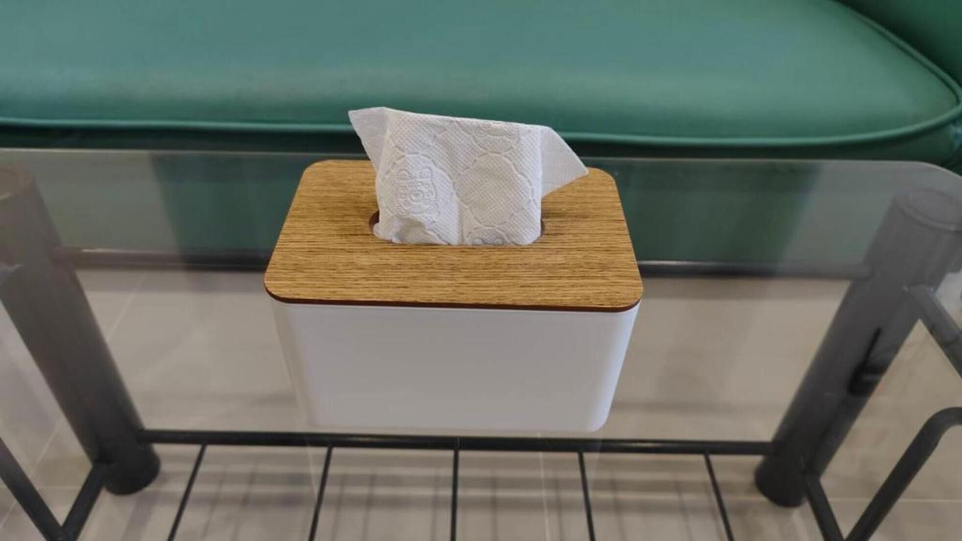 Une boîte de mouchoirs sur une table en verre, avec un canapé vert en arrière-plan.