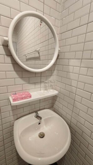 A bathroom with a white sink, a mirror, and a shelf with a pink soap dispenser. - Keerana Villa (Bueang Sam Phan)