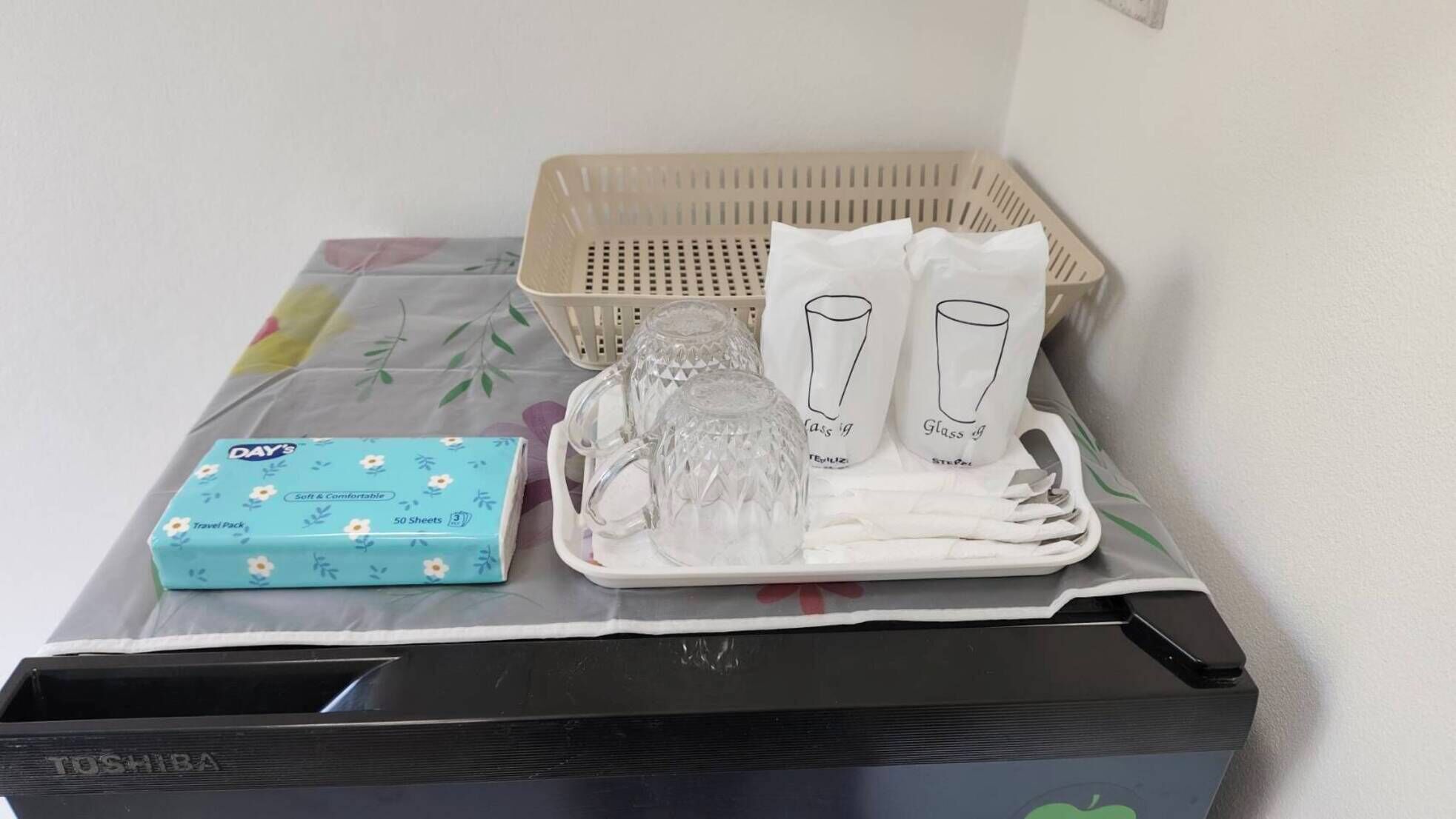 Una caja con la marca Toshiba, un kit de viaje, una taza de vidrio y una copa de vidrio sobre una mesa.