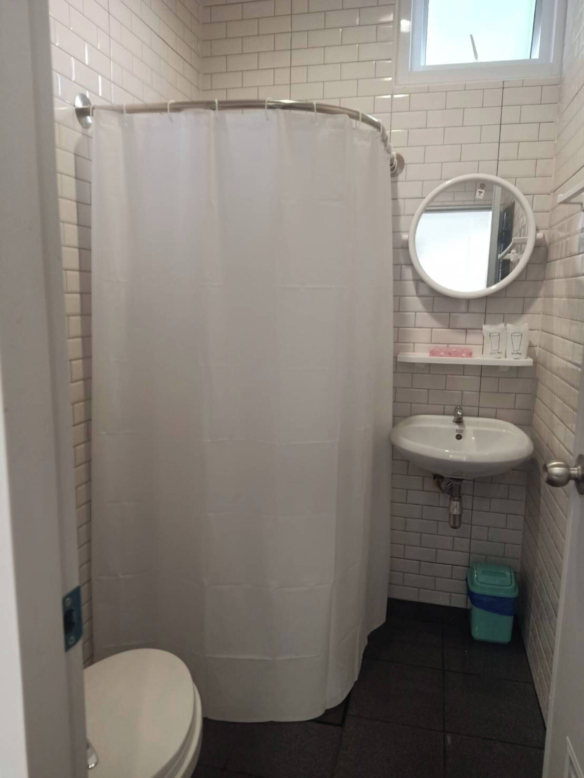 Un baño pequeño con cortina de ducha, inodoro, lavamanos y ventana.