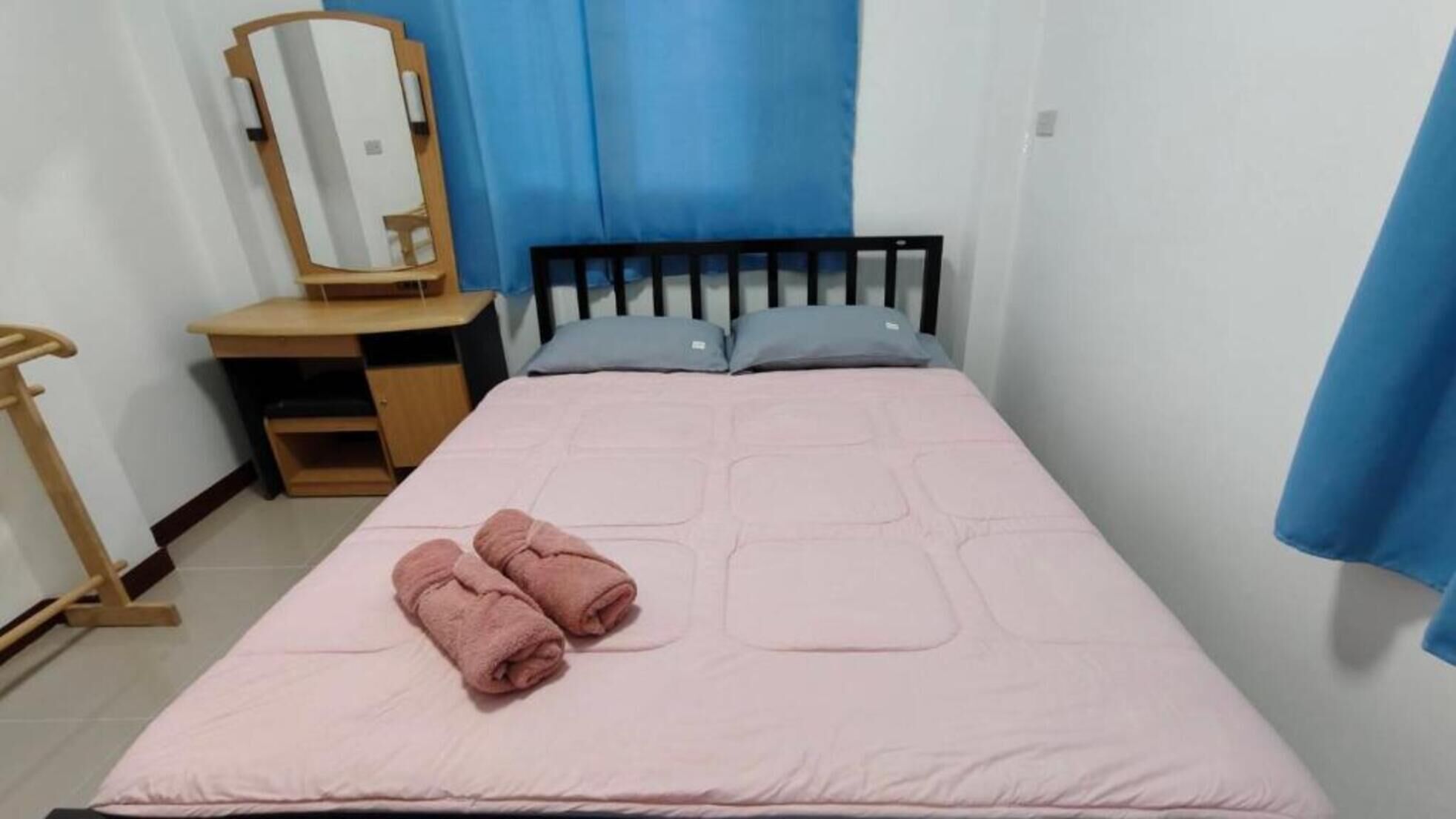 Quarto com cama, mesa de cabeceira de madeira, espelho e cortinas azuis.