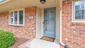 A brick house with a blue door, a number 5110 sign, and a welcome mat. - *Pet Friendly* Charming-Single story | Fenced Yard, Outdoor Dining, Near Duke (Durham)