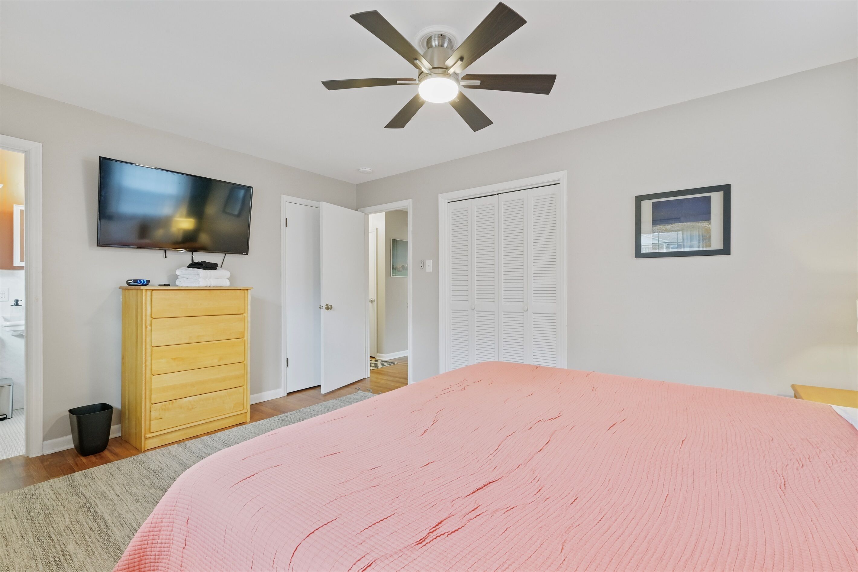 Een slaapkamer met een bed, een plafondventilator, een televisie, een houten dressoir en een kast.