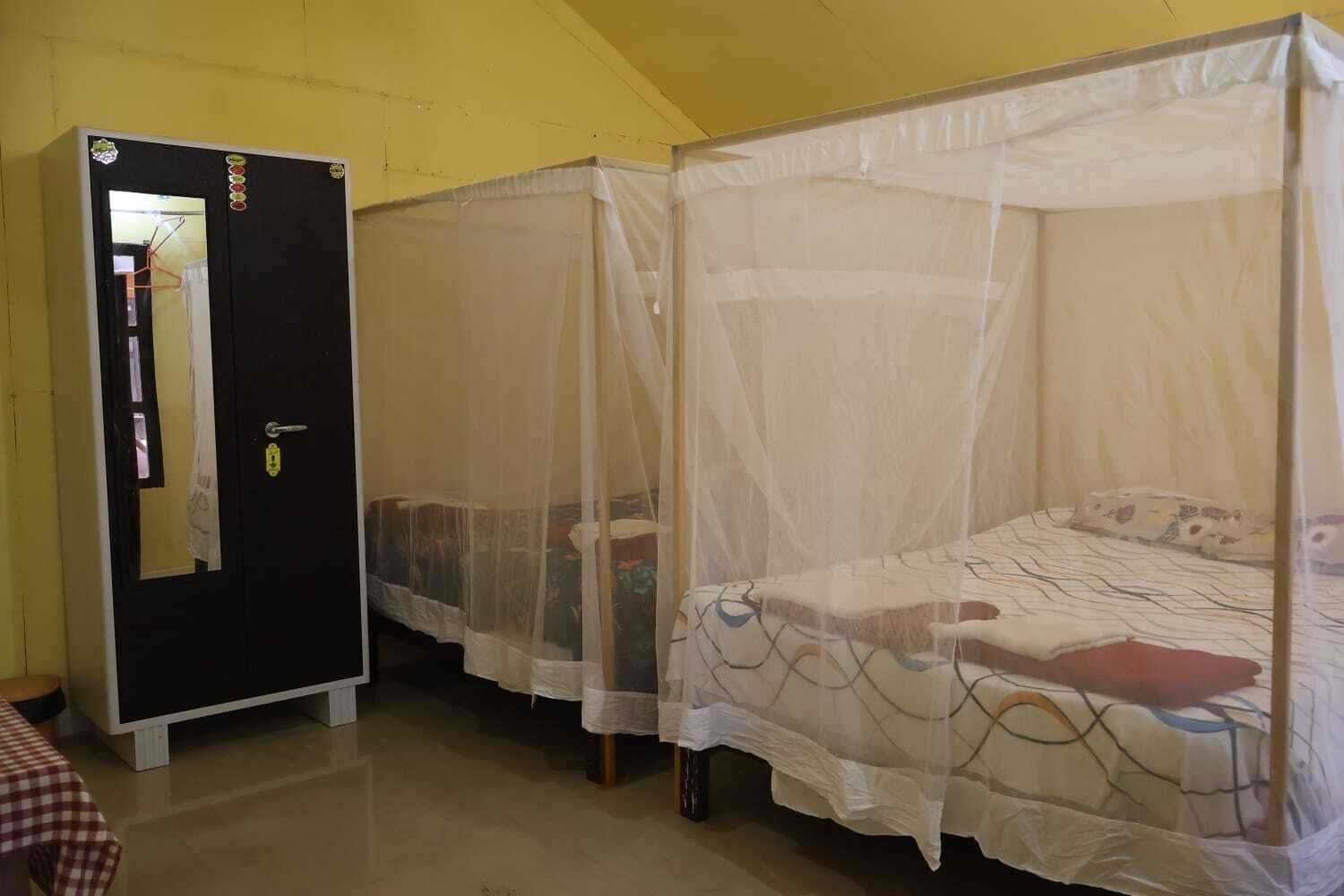 A room with two beds covered by mosquito nets, a black wardrobe, and a checkered tablecloth.