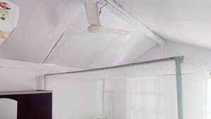 A room with a bed covered by a mosquito net, a ceiling fan, and a wardrobe. - Nirvana Beach Cottages (Canacona)