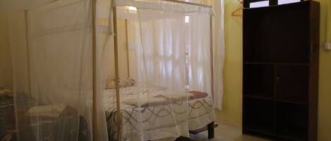 Una habitación con dos camas individuales, cada una con dosel, un armario de madera y un tapiz de cuadros en el suelo.