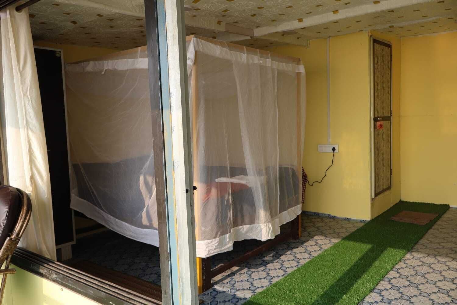 Une pièce avec un lit recouvert d’une moustiquaire, une chaise et un petit tapis.
