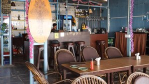A restaurant with a bar area, wooden tables, wicker chairs, and hanging decorations. - Nirvana Beach Cottages (Canacona)