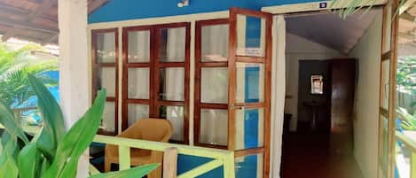Un espacio al aire libre techado, con pared azul, ventanas de madera y barandilla amarilla.