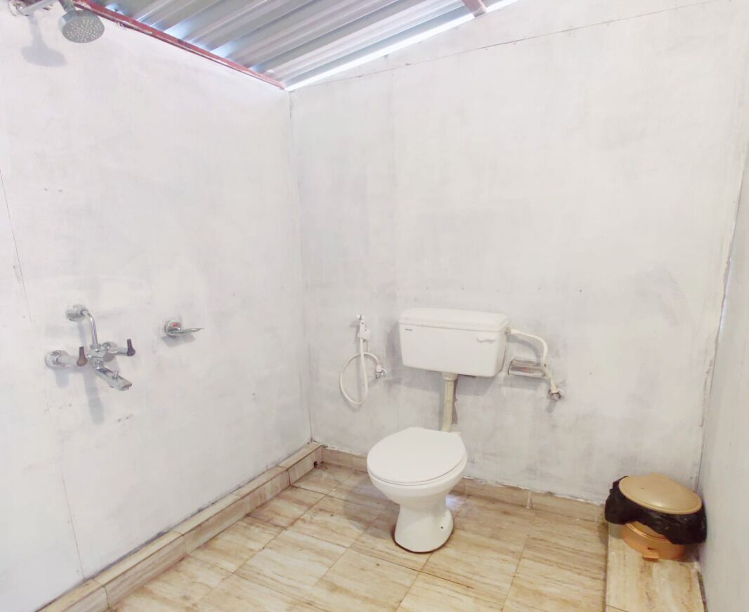 A small, white-walled bathroom with a toilet, a showerhead, and a toilet paper holder.