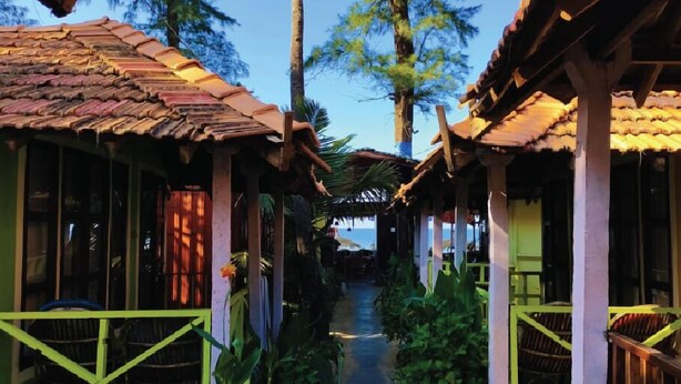 A corridor with thatched-roof huts, a pathway, and tropical vegetation. - Nirvana Beach Cottages (Canacona)