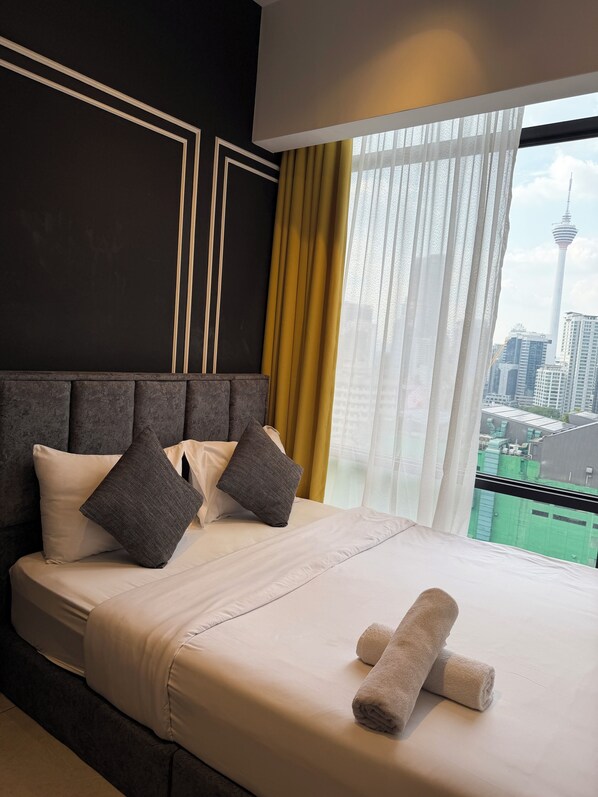 A hotel room with a large bed, two pillows, a neatly folded towel, and a view of a cityscape with a tower. - AXON RESIDENCE BY PERKASA IKON (Kuala Lumpur)