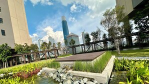 A rooftop garden with a small pond, surrounded by greenery and a metal bridge.