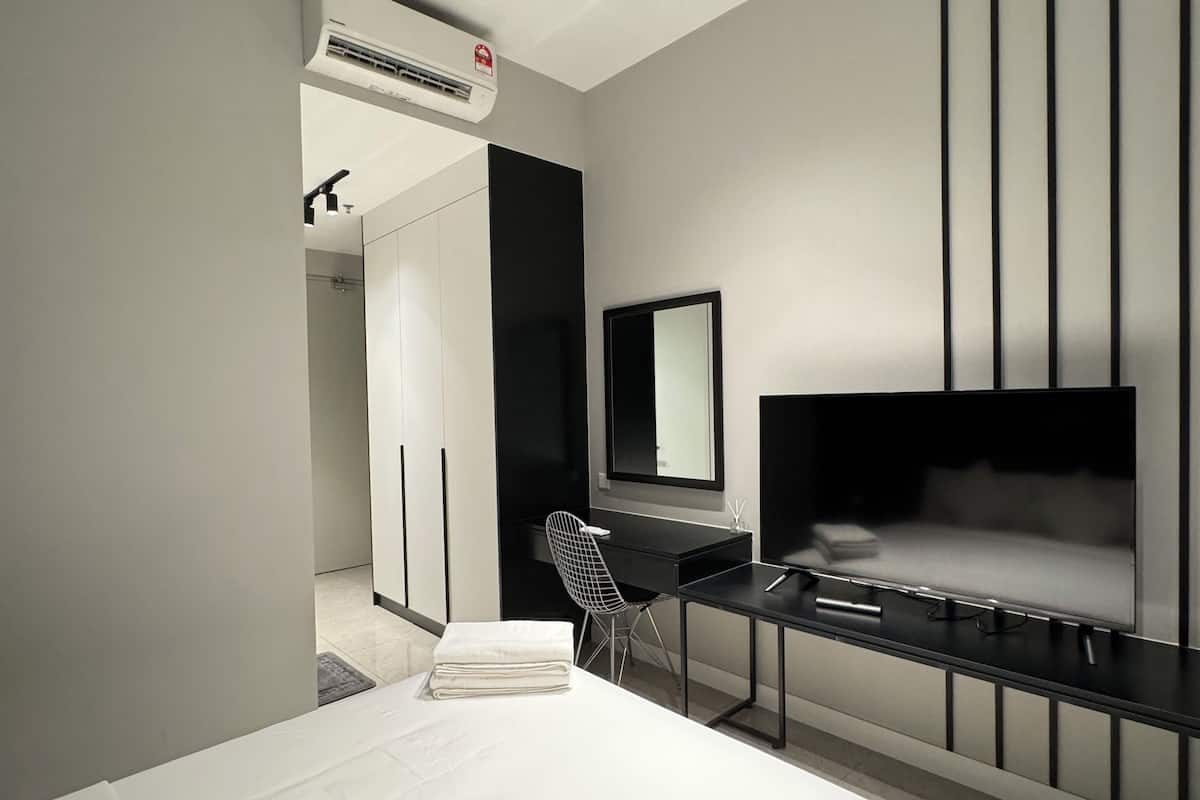A modern hotel room with a large bed, a desk with a chair, a flat-screen TV, and a large mirror.