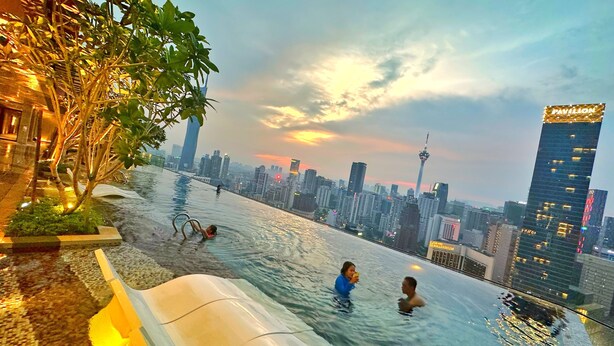 An infinity pool with a city skyline view, surrounded by greenery and modern buildings.