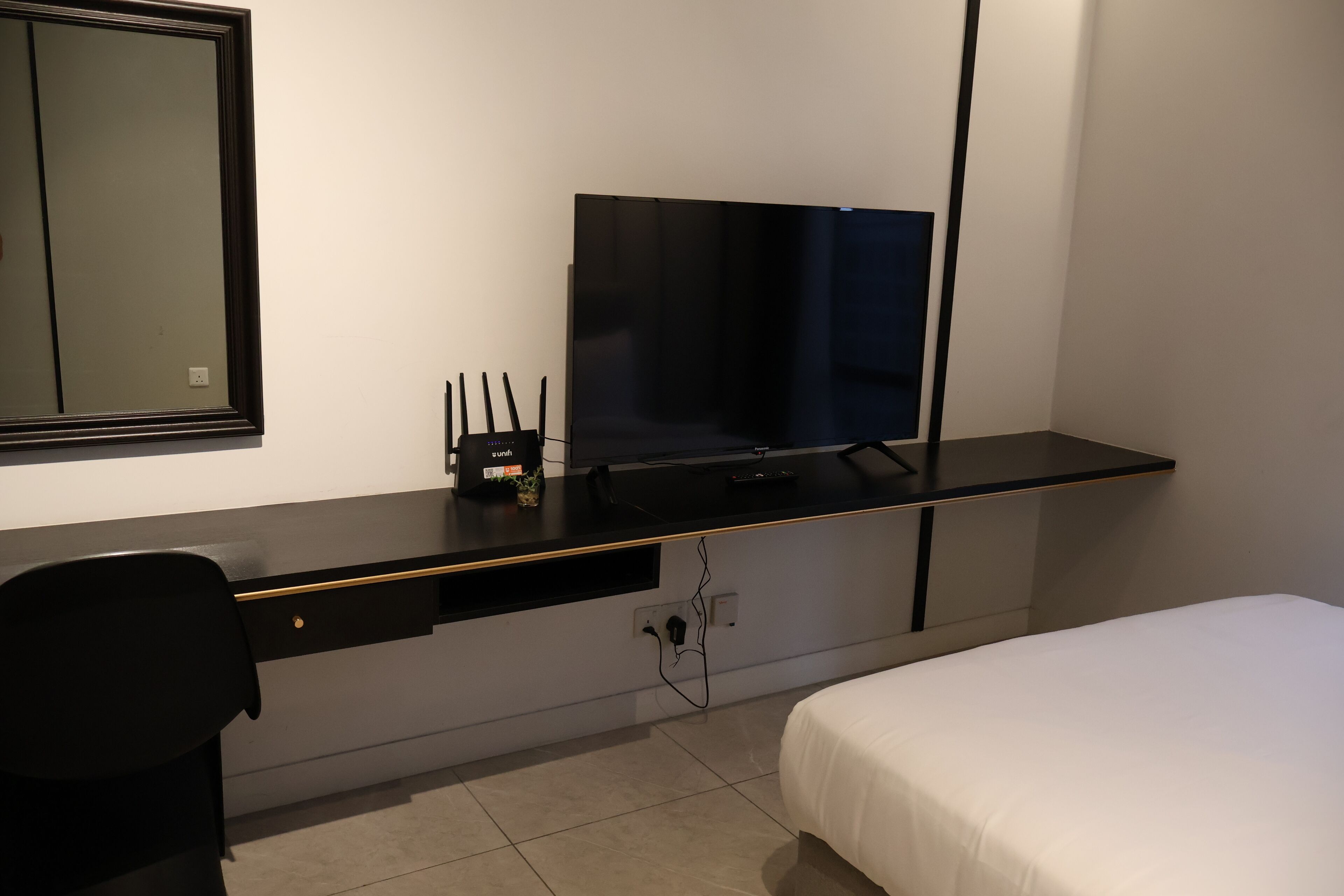 Une chambre d’hôtel comprenant un lit, un bureau avec un téléviseur à écran plat, une chaise et une petite table avec une plante.