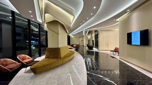 A modern lobby with a curved reception desk, plush seating, and a large digital display on the wall.