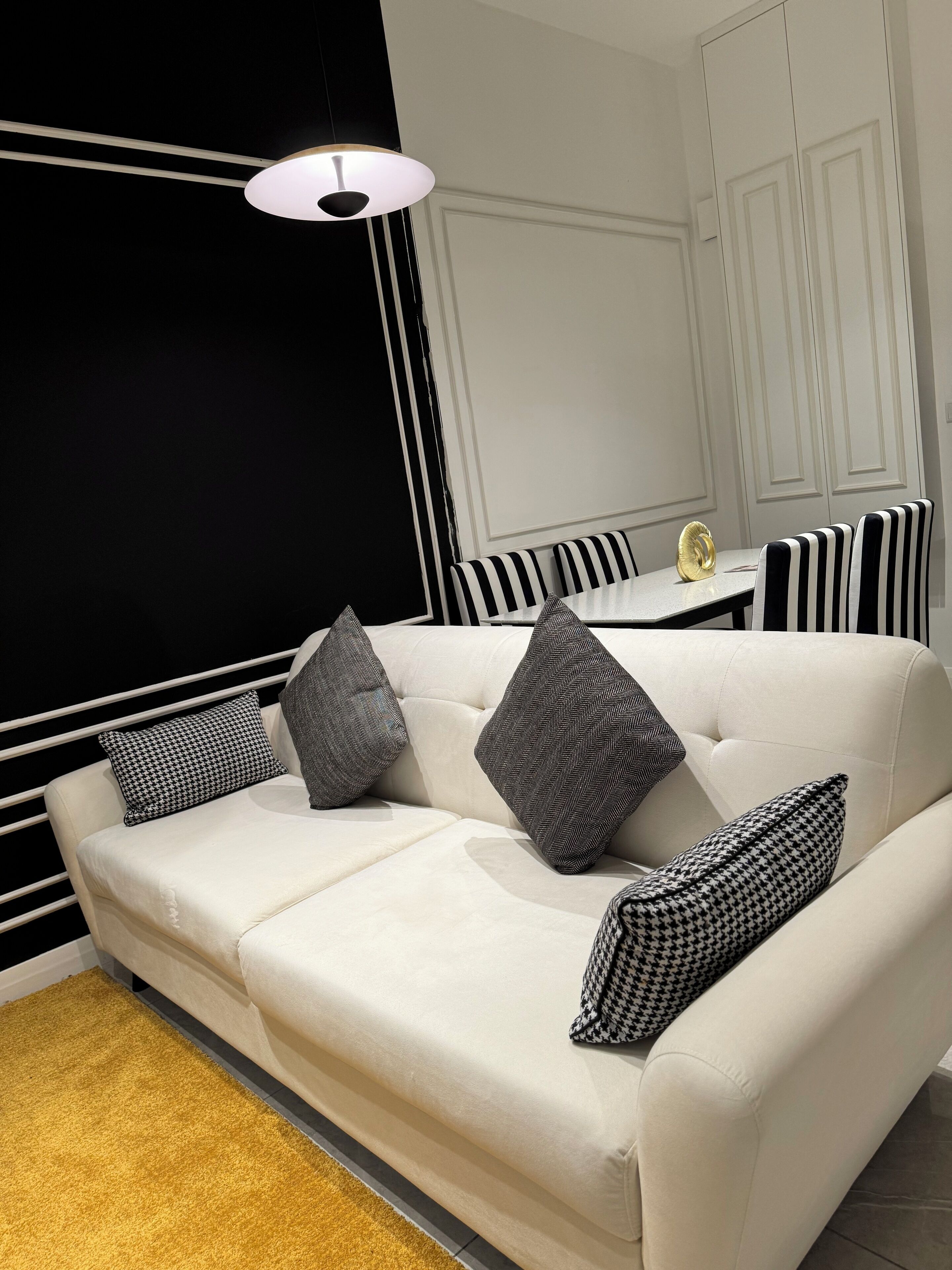 A modern living room with a white sofa, black and white striped chairs, and a gold decorative object on the table.
