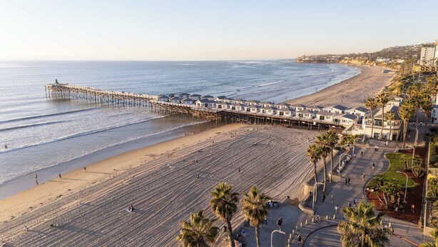 A beach with a wooden pier extending into the ocean, lined with houses and palm trees. - 2 Units in One! |  Walk to the Beach & Boardwalk (San Diego)