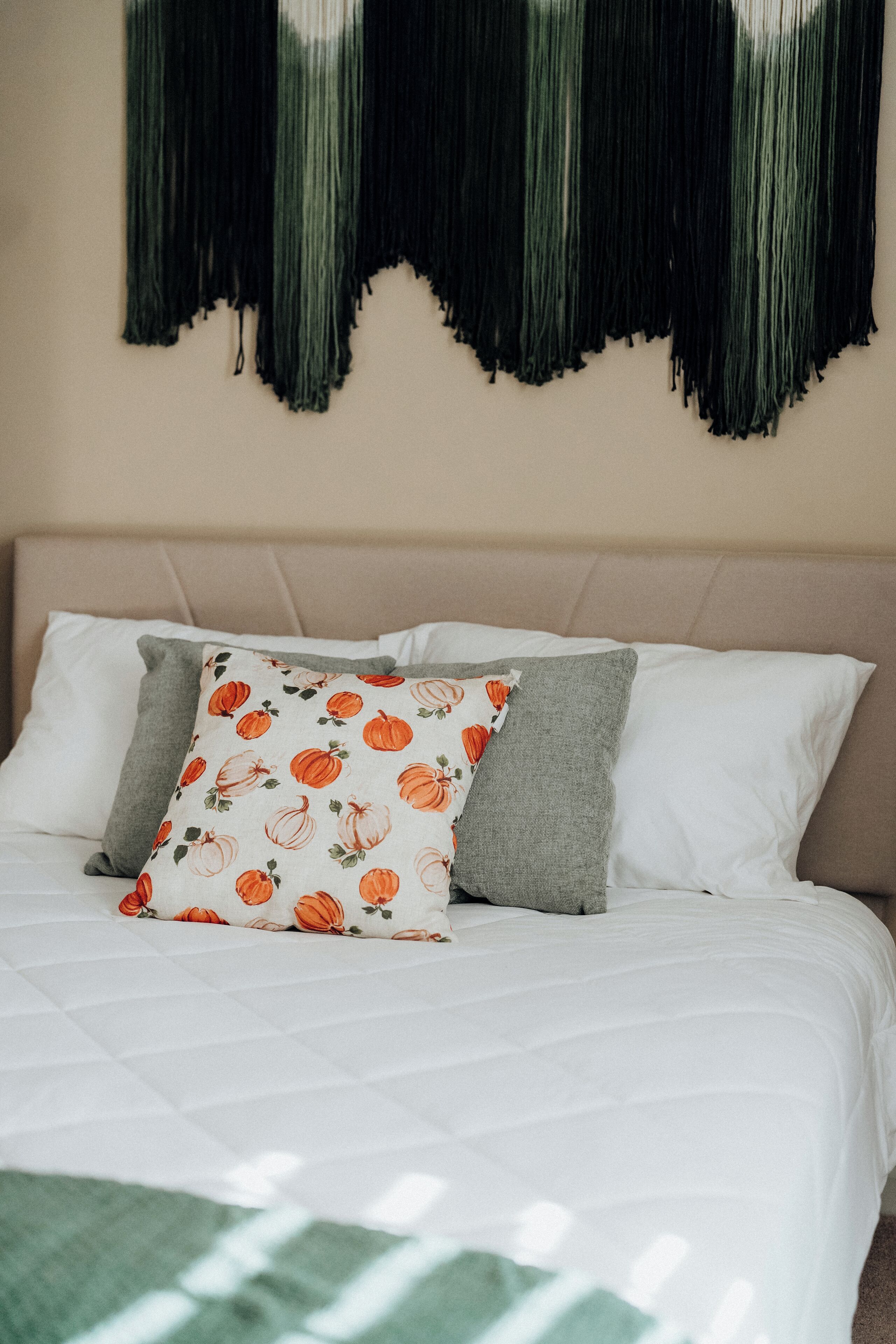 Cama com roupa de cama branca e almofada com padrão de abóbora.